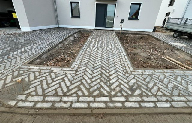Driveway in light and dark clay pavers laid in a herringbone bond in front of a new build