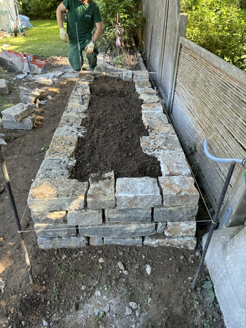 Raised bed built from shell limestone blocks, a Holste Garten team member filling in the growing medium