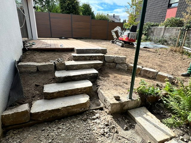 Natural stone steps and dry stone wall securing a slope beside a timber deck, mini excavator on site
