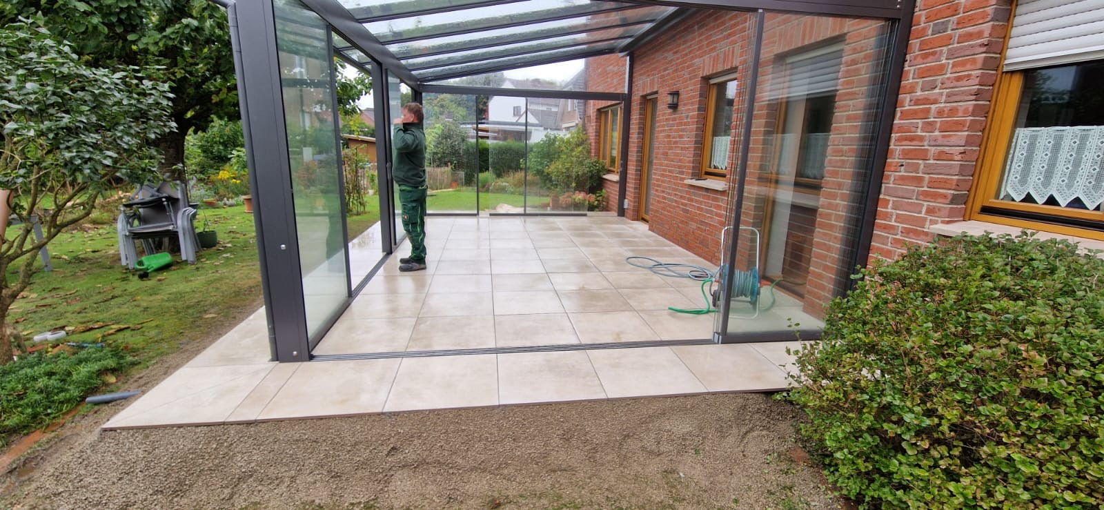 Glass and aluminium terrace roof over a porcelain stoneware terrace, Holste Garten team member on final inspection