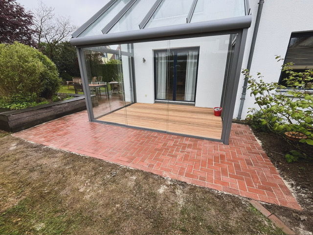 Glass terrace roof with a timber deck inside and red clay pavers in herringbone bond in front